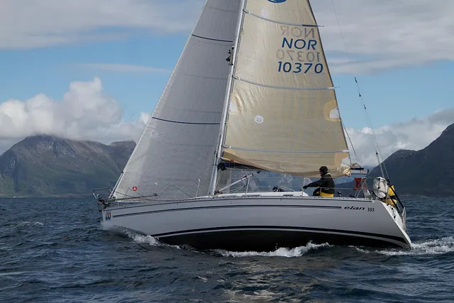 Enslig seilbåt på havet med disige fjell i bakgrunnen.