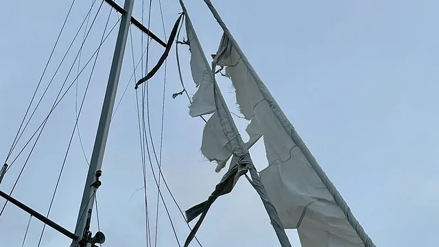Mast på seilbåt med ødelagt og revet seil hengende i riggen.